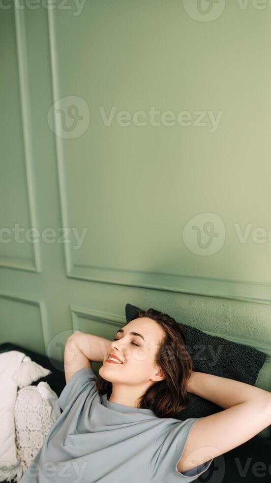 A smiling young woman with her eyes closed is lying on a couch, enjoying some rest and sleep. Serenity Unveiled. Relaxed Young Woman Rests Peacefully on Sofa. Blissful Slumber photo
