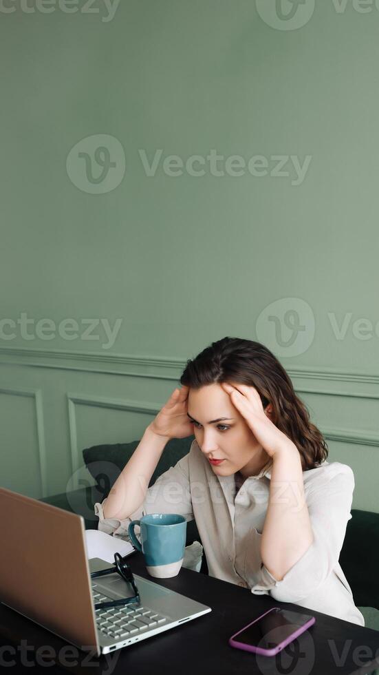 Stressful Workday. Tired Woman Coping with Fatigue and Health Issues. Exhausted Woman Struggling with Fatigue, Blood Pressure, and Headaches While Staring at Laptop photo