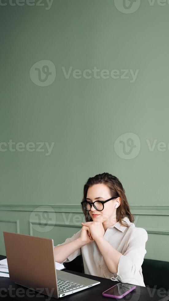 Connected and Smiling. Woman with Wireless Headphones Engages in Laptop Video Call with Joy. Digital Conversation. Woman in Goggles Smiles During Laptop Video Chat photo