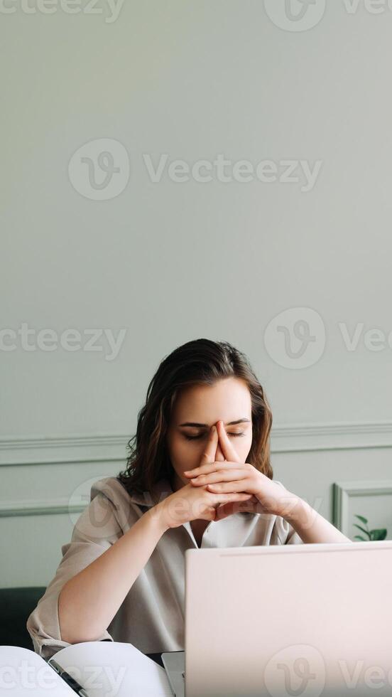 Stressed and Overworked Young Woman with Laptop, Battling Fatigue, Pressure, Migraine, and Stress. Modern Work Challenges. Sad Woman Suffering from Overwork. Tired and Unhappy. photo