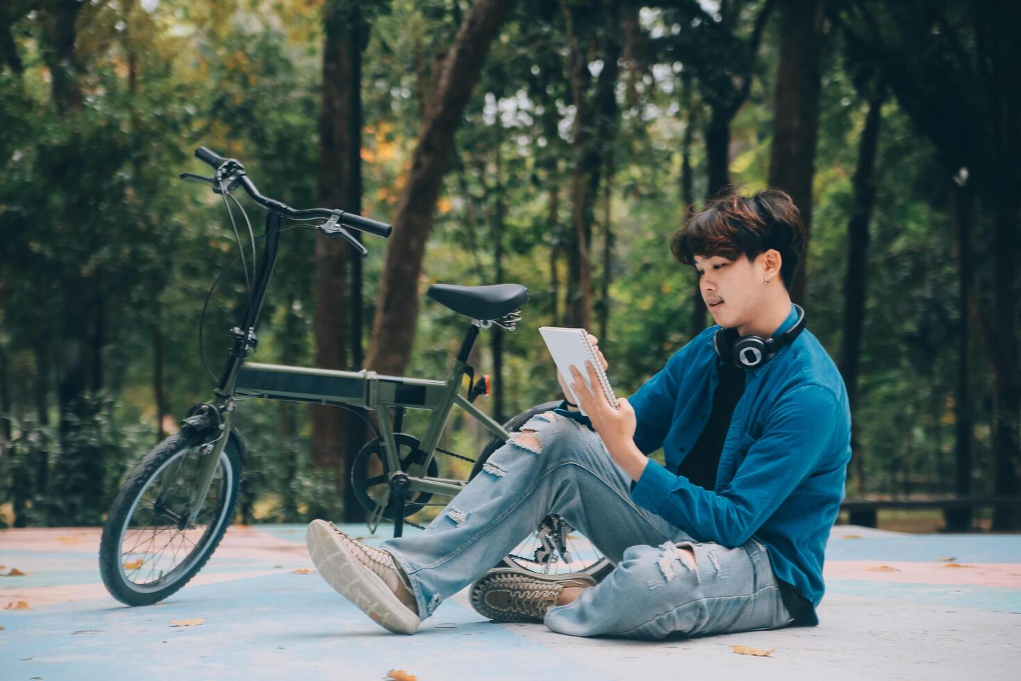 Young handsome bearded man taking a break while travelling the city with his bicycle using his digital tablet looking away thoughtfully photo