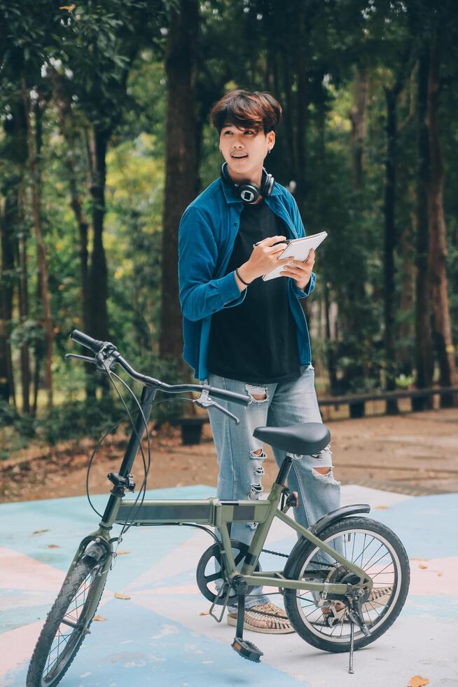 Young handsome bearded man taking a break while travelling the city with his bicycle using his digital tablet looking away thoughtfully photo