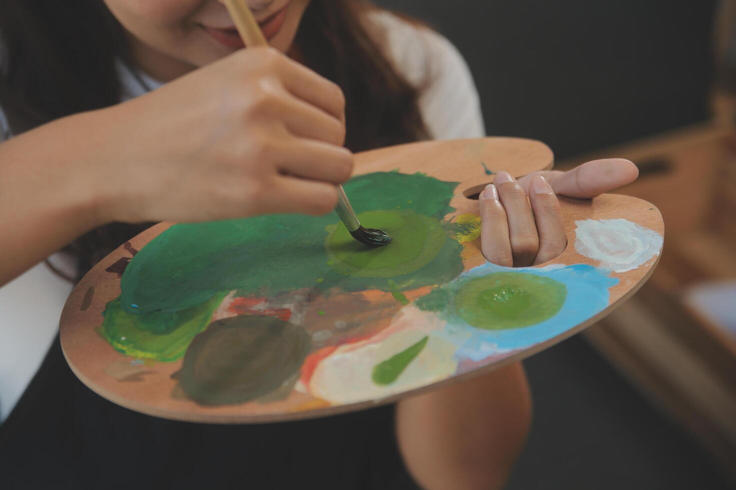 Cropped image of female artist standing in front of an easel and dipping brush into color palette photo