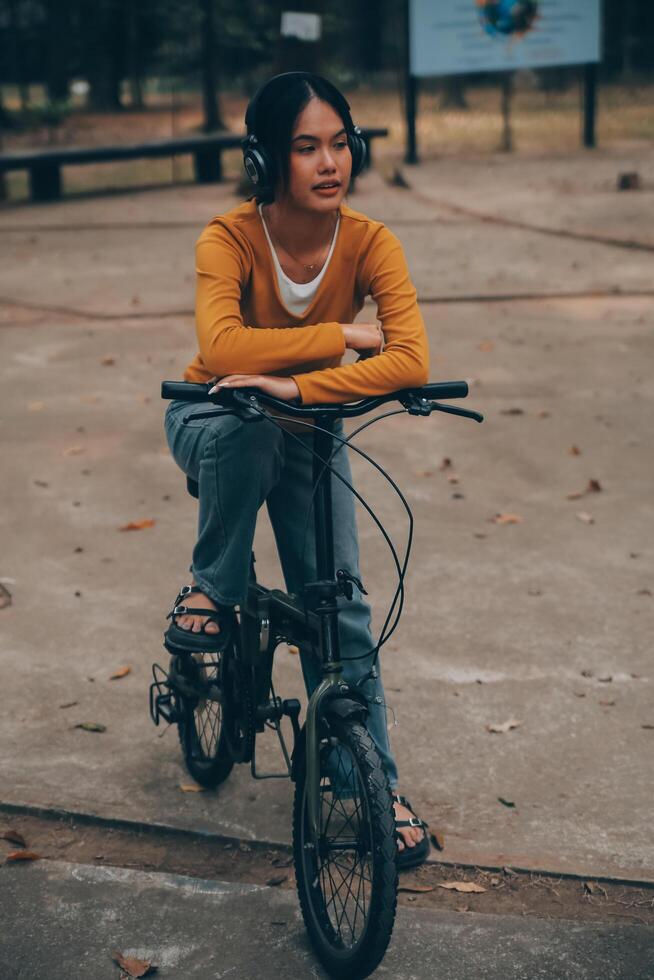 Happy young Asian woman while riding a bicycle in a city park. She smiled using the bicycle of transportation. Environmentally friendly concept. photo