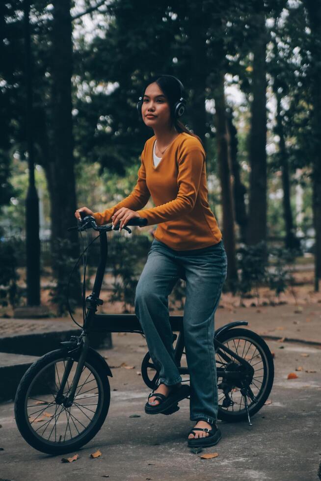 Happy young Asian woman while riding a bicycle in a city park. She smiled using the bicycle of transportation. Environmentally friendly concept. photo