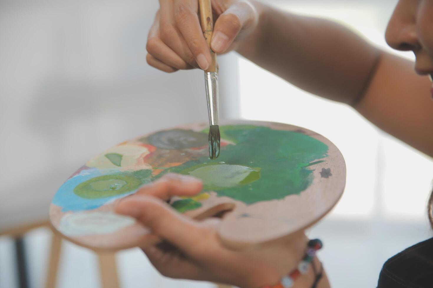 Cropped image of female artist standing in front of an easel and dipping brush into color palette photo