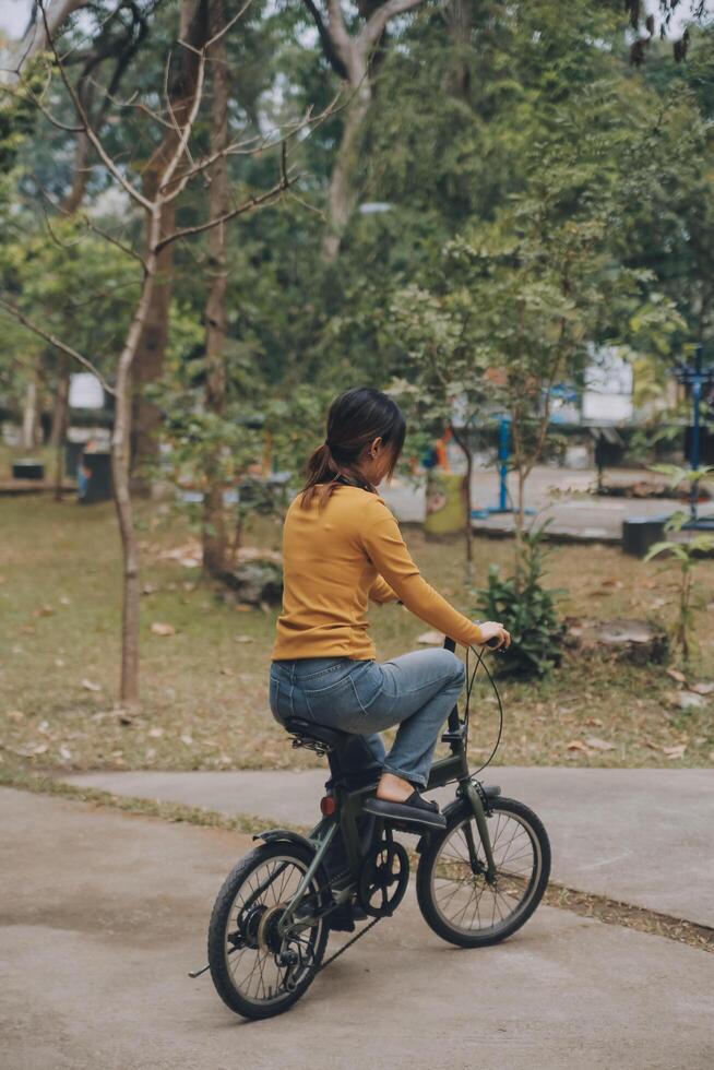 Happy young Asian woman while riding a bicycle in a city park. She smiled using the bicycle of transportation. Environmentally friendly concept. photo