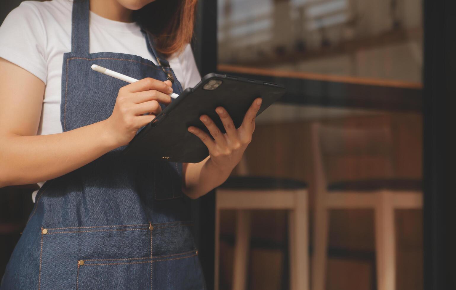 Startup successful small business owner sme beauty girl stand with tablet smartphone in coffee shop restaurant. Portrait of asian tan woman barista cafe owner. SME entrepreneur seller business concept photo