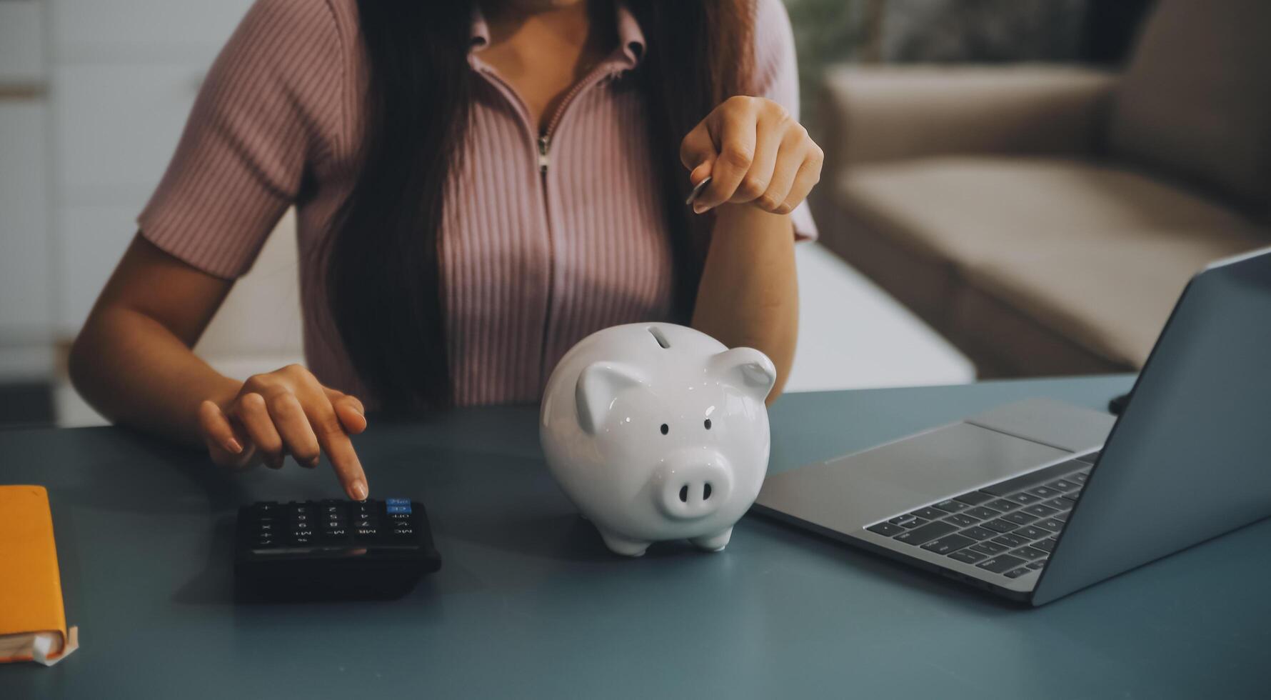 Young Asian woman saving for retirement Saving money through a piggy bank and taking notes on notebook, savings concept. photo