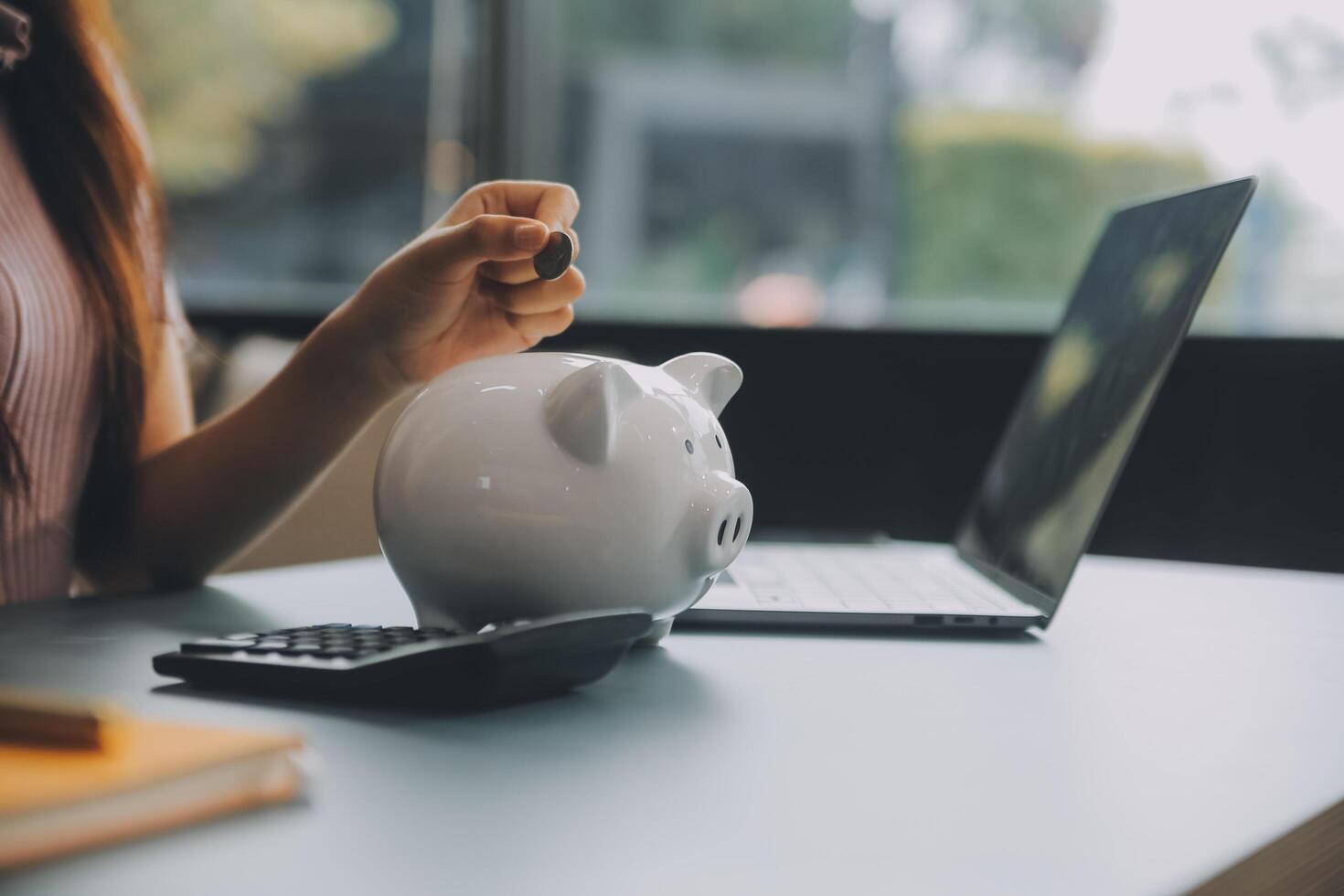 Young Asian woman saving for retirement Saving money through a piggy bank and taking notes on notebook, savings concept. photo