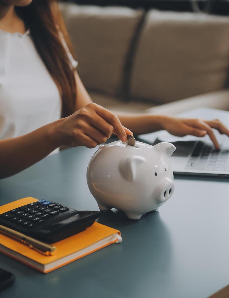 Young Asian woman saving for retirement Saving money through a piggy bank and taking notes on notebook, savings concept. photo