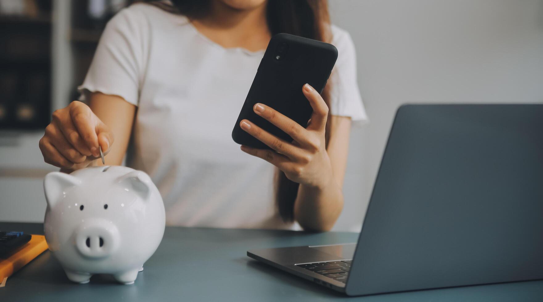 Young Asian woman saving for retirement Saving money through a piggy bank and taking notes on notebook, savings concept. photo