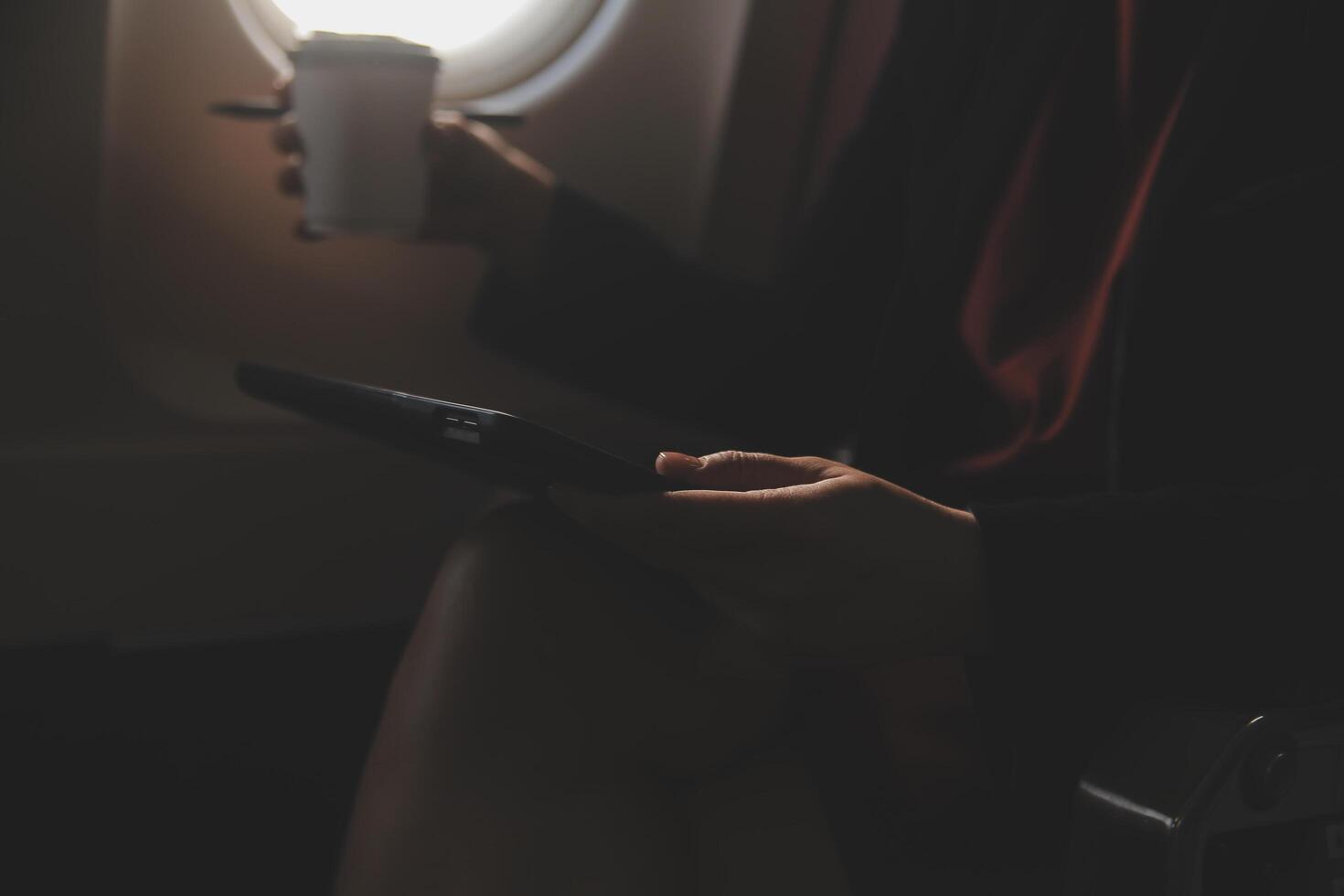 Blonde female tourist checking incoming notification on smartphone sitting on seat of airplane with netbook.Young businesswoman share media from telephone on laptop computer during plane flight photo