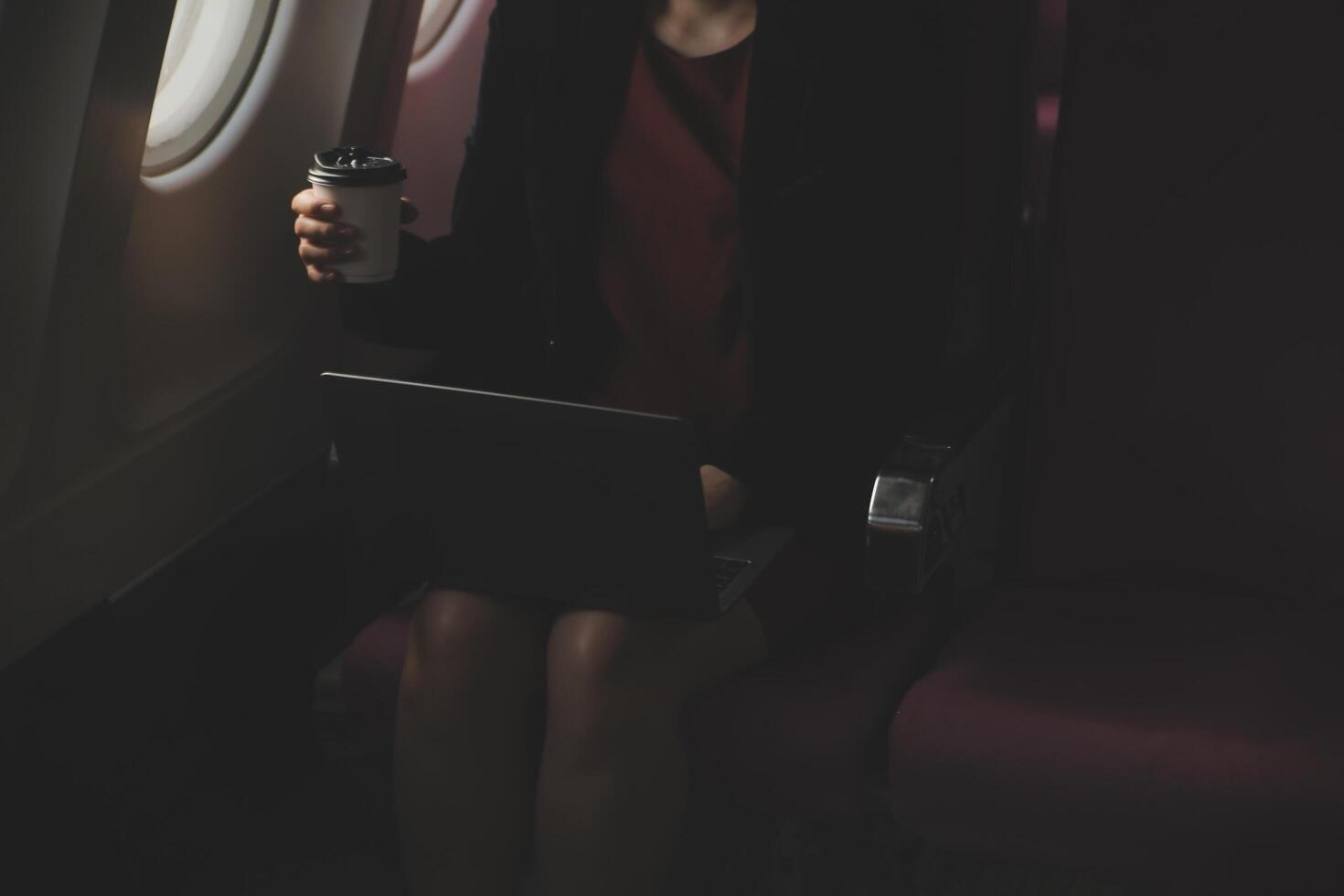 Blonde female tourist checking incoming notification on smartphone sitting on seat of airplane with netbook.Young businesswoman share media from telephone on laptop computer during plane flight photo