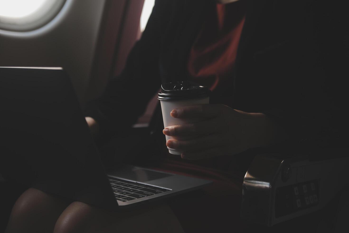 Blonde female tourist checking incoming notification on smartphone sitting on seat of airplane with netbook.Young businesswoman share media from telephone on laptop computer during plane flight photo