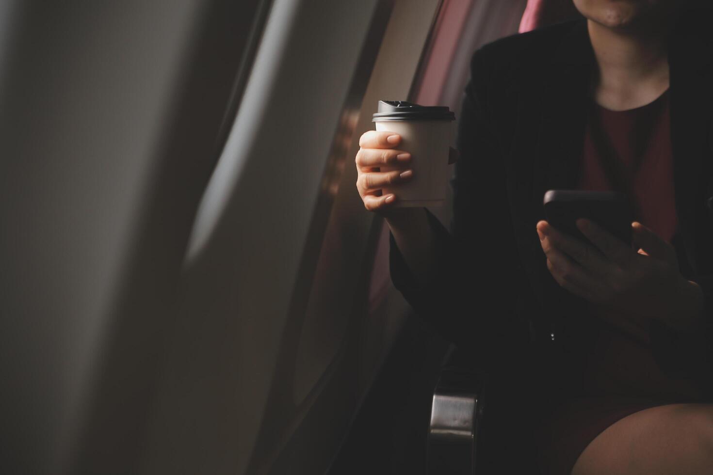 Blonde female tourist checking incoming notification on smartphone sitting on seat of airplane with netbook.Young businesswoman share media from telephone on laptop computer during plane flight photo