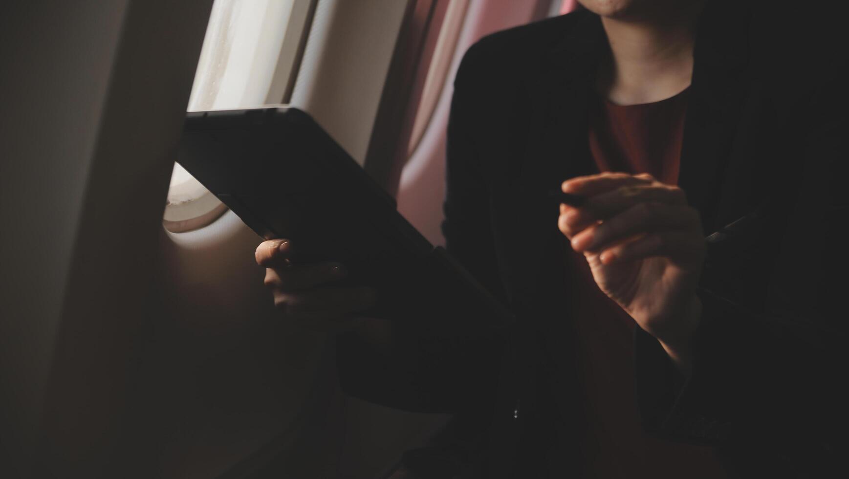 Blonde female tourist checking incoming notification on smartphone sitting on seat of airplane with netbook.Young businesswoman share media from telephone on laptop computer during plane flight photo