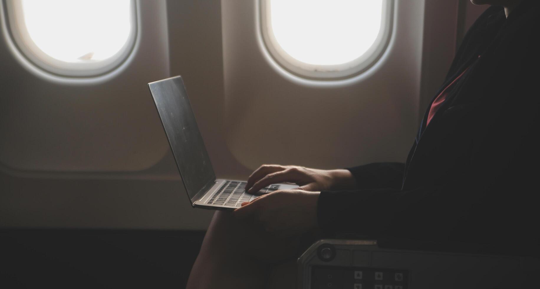 Blonde female tourist checking incoming notification on smartphone sitting on seat of airplane with netbook.Young businesswoman share media from telephone on laptop computer during plane flight photo