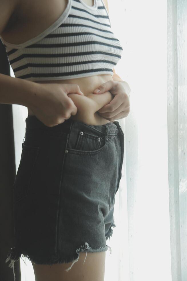 Women body fat belly. Obese woman hand holding excessive belly fat. diet lifestyle concept to reduce belly and shape up healthy stomach muscle. photo