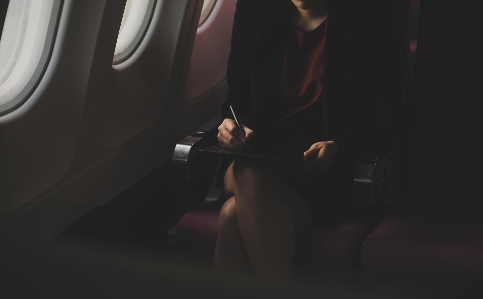 Blonde female tourist checking incoming notification on smartphone sitting on seat of airplane with netbook.Young businesswoman share media from telephone on laptop computer during plane flight photo