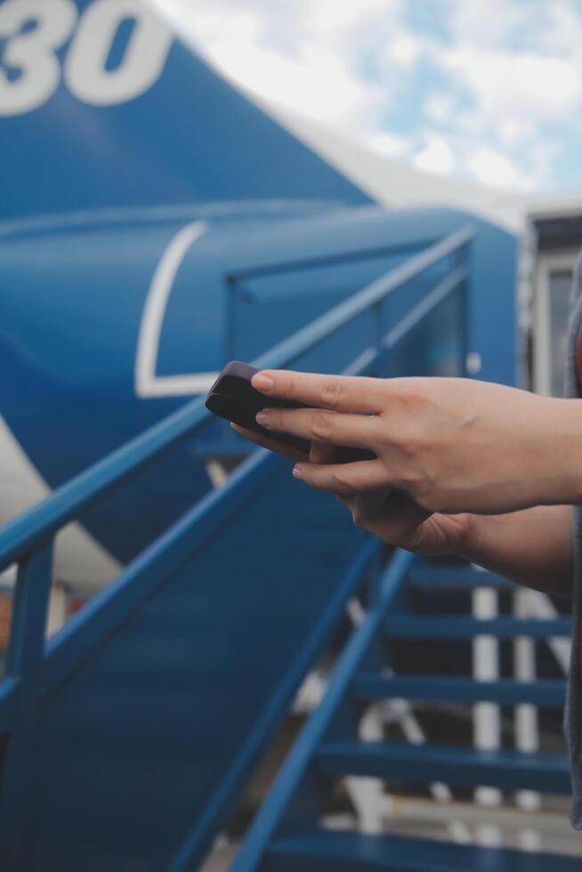 Blonde female tourist checking incoming notification on smartphone sitting on seat of airplane with netbook.Young businesswoman share media from telephone on laptop computer during plane flight photo