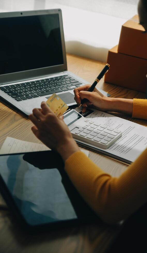 Young woman holding a smartphone, tablet showing payment success and credit card with yellow parcel box as online shopping concept in office photo
