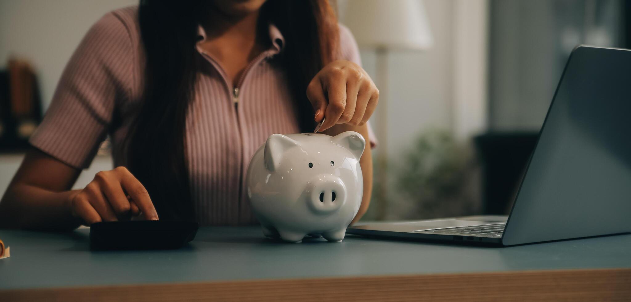 Young Asian woman saving for retirement Saving money through a piggy bank and taking notes on notebook, savings concept. photo