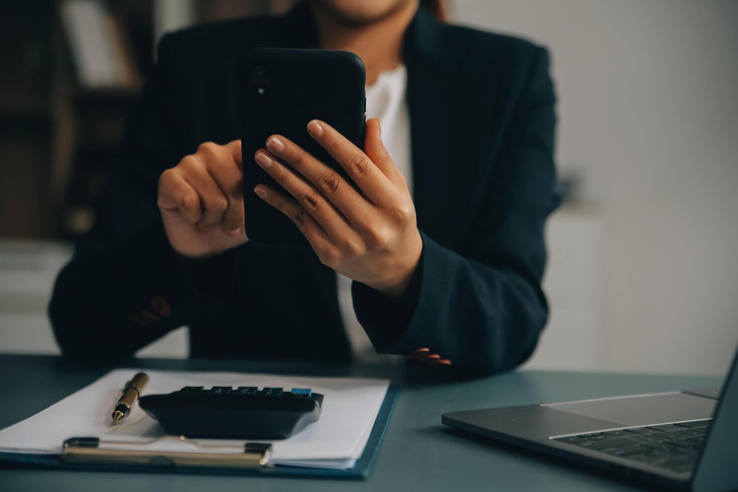 Hispanic businesswoman in formal attire in her office happy and cheerful while using smartphones and working. Young businesswoman using apps on cell phones, reading news, fast connection photo