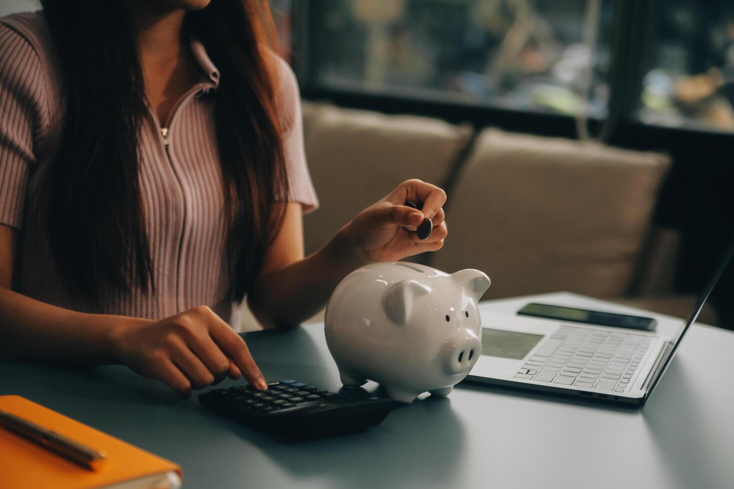 Young Asian woman saving for retirement Saving money through a piggy bank and taking notes on notebook, savings concept. photo