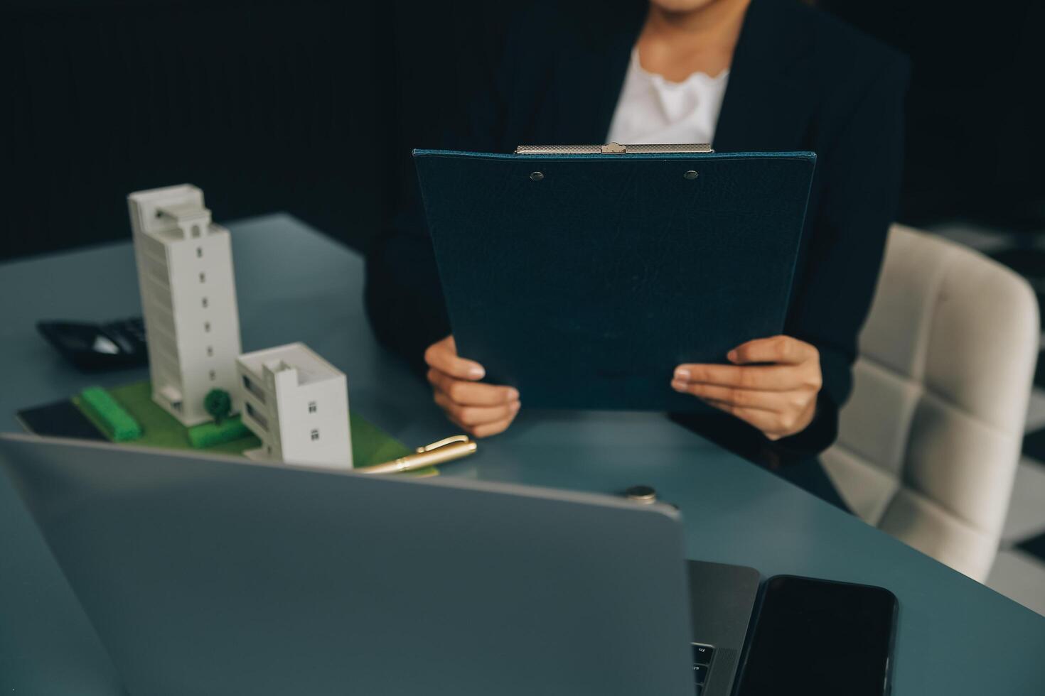 Close up realtor sit at table holds tiny house model, layout of cottage. Real estate purchase, new property, ownership, construction company make special offer to client, affordable dwelling concept photo