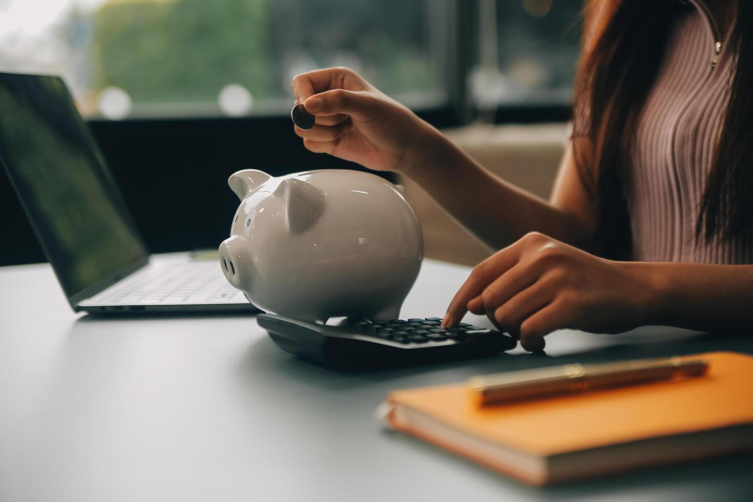 Young Asian woman saving for retirement Saving money through a piggy bank and taking notes on notebook, savings concept. photo