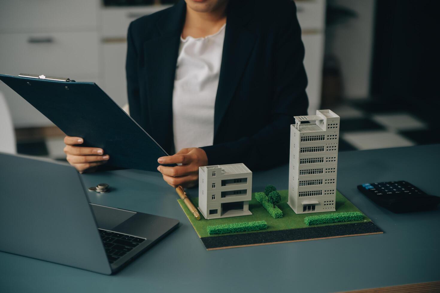 Close up realtor sit at table holds tiny house model, layout of cottage. Real estate purchase, new property, ownership, construction company make special offer to client, affordable dwelling concept photo