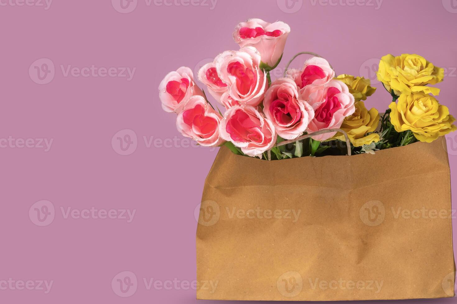 Bouquet of pink and yellow tulips in a paper bag on a purple background with copy space for your text photo