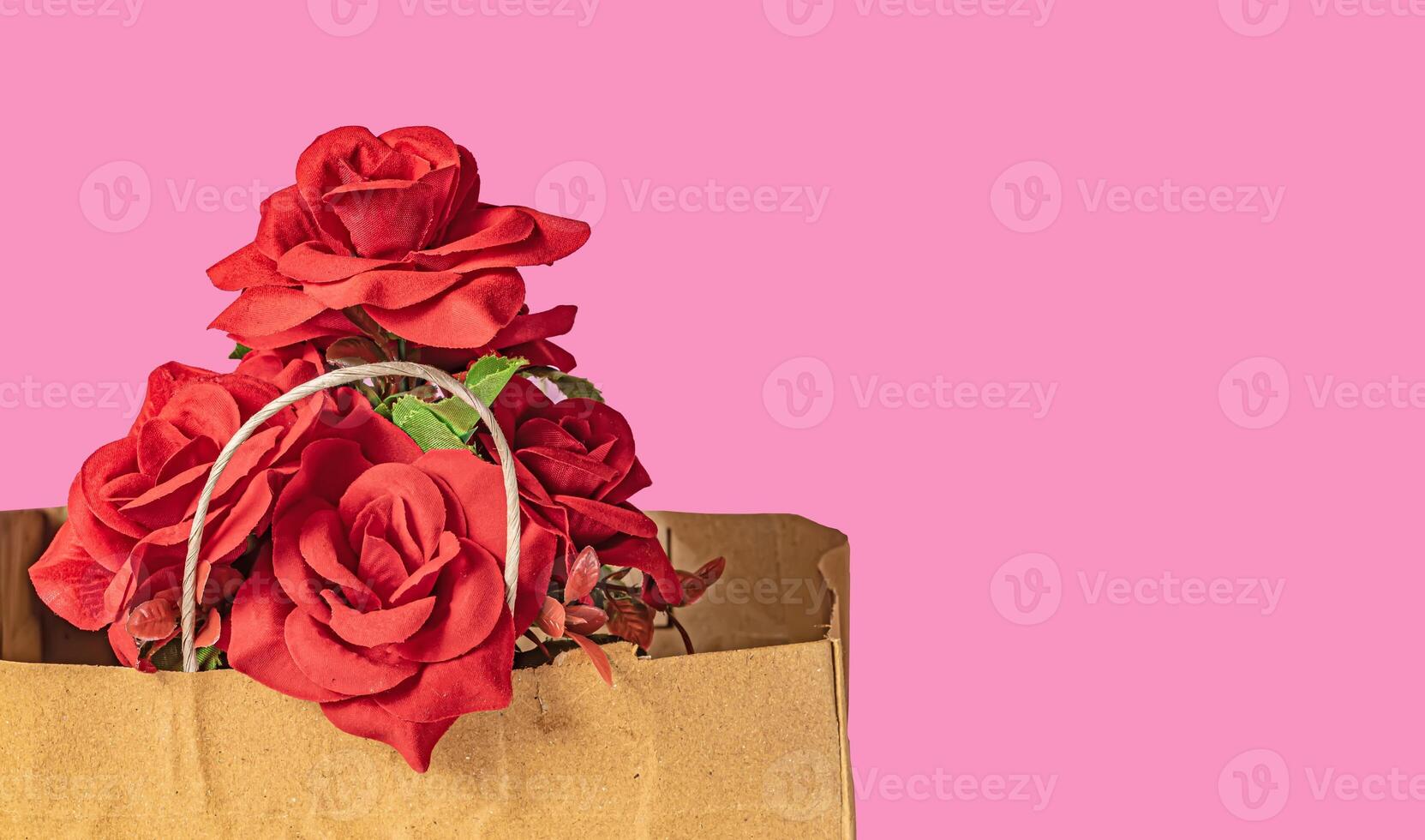 Bouquet of red roses in a brown paper bag on a pink background for Valentine's Day with copy space for your text. photo