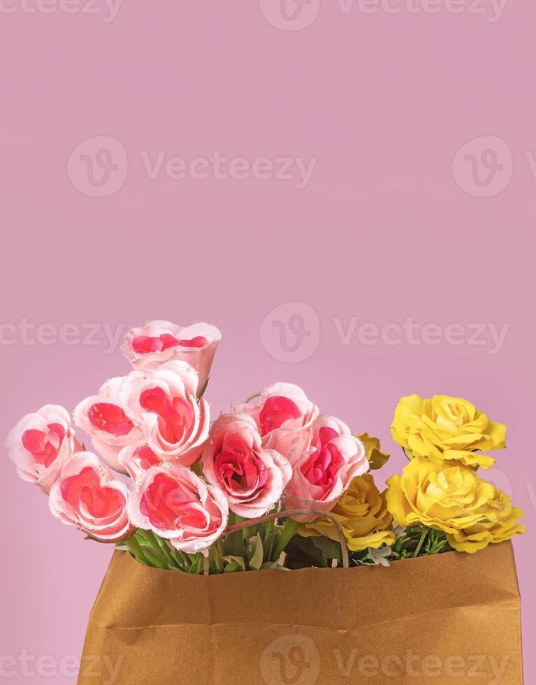 Valentine's Day concept. Bouquet of pink and yellow roses in paper bag on pink background photo
