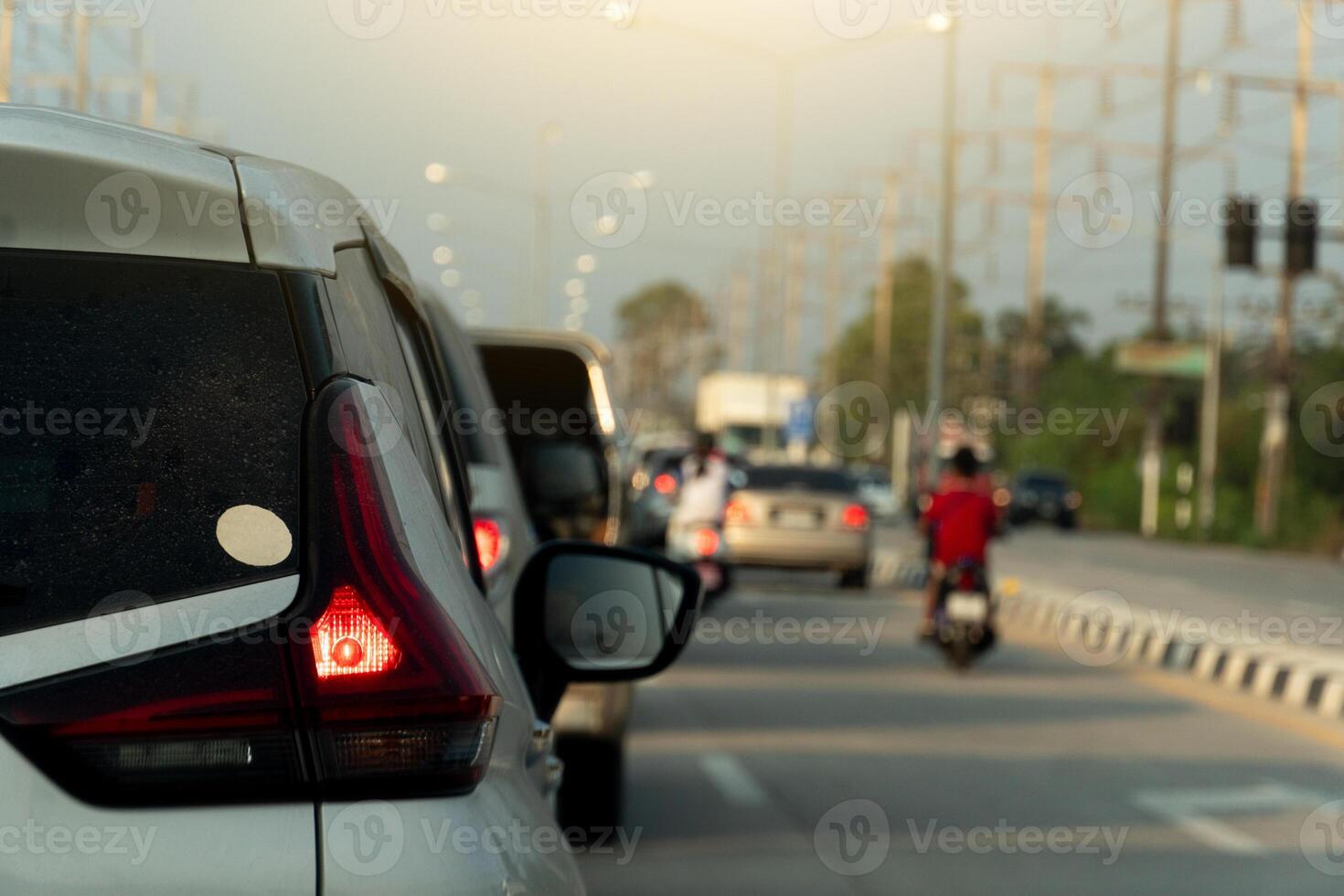 Transport of car on the concrete road. Rear side of white car with turn on brake light. Many cars parking in a long queue in the city. photo