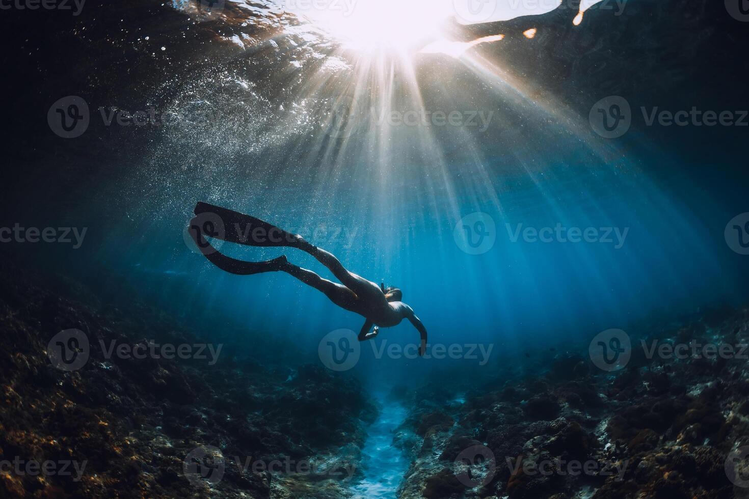 Young freediver woman with fins glides and amazing sun rays. Freediving underwater in ocean photo