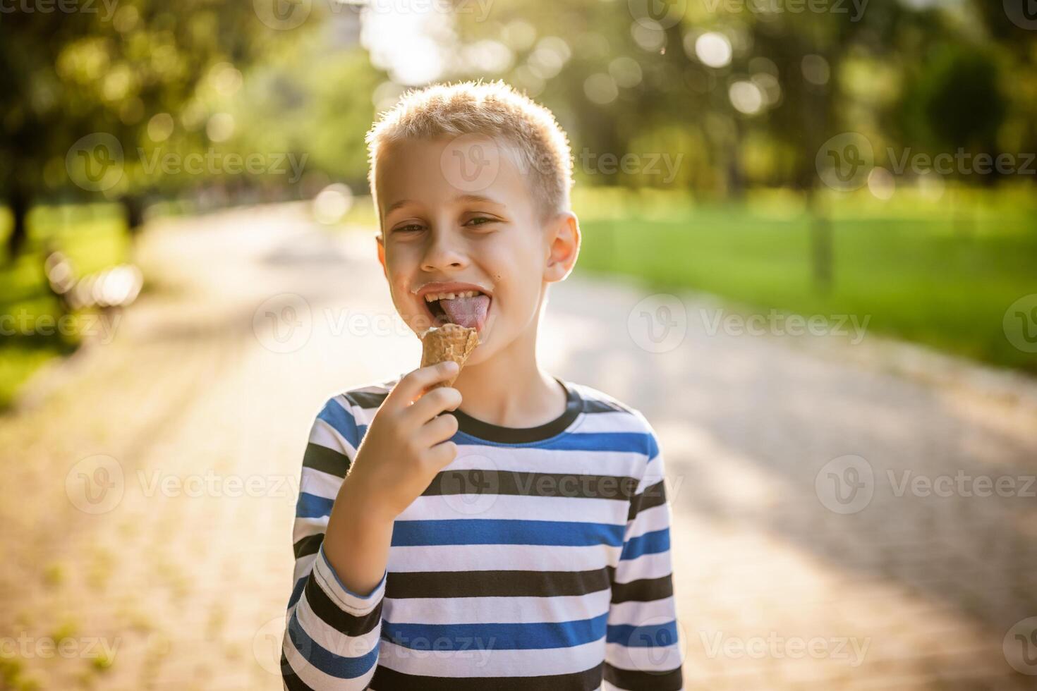 Portrait of happy boy who is standing in park and eating ice cream. photo