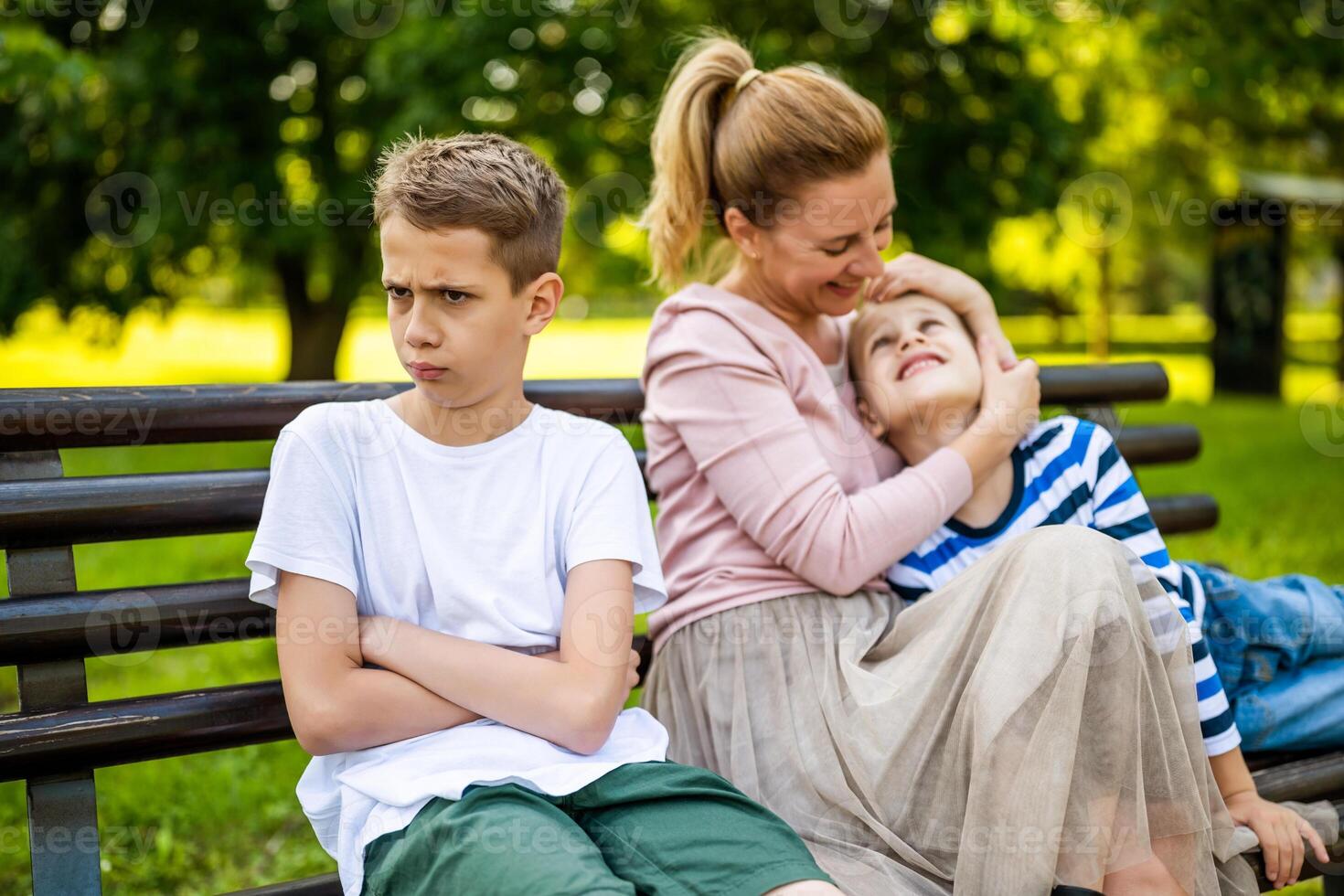 contento madre es sentado con su hijos en banco en parque. uno chico es ofendido y haciendo pucheros foto