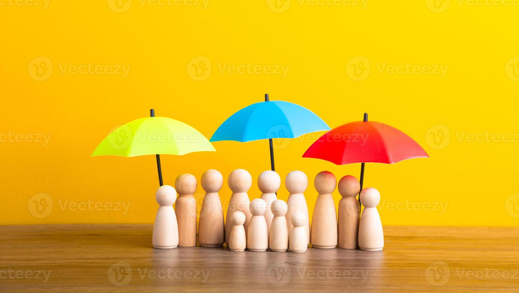 Many wooden people figures under umbrella on yellow background. photo