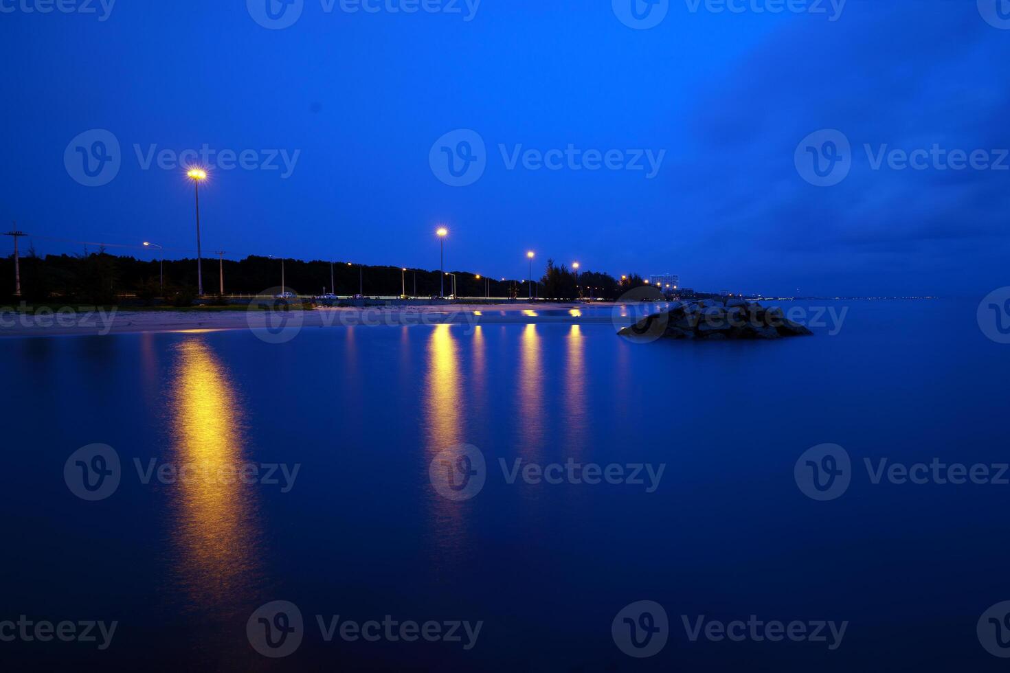 The road follows the coast at dusk and is lit by light poles photo