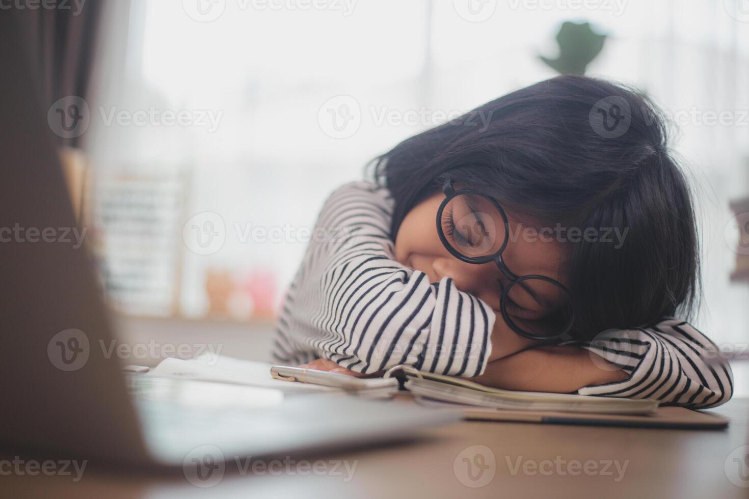 Little Asian girl sitting alone and looking out with a bored face, Preschool child laying head down on the table with sad bored with homework, spoiled child photo