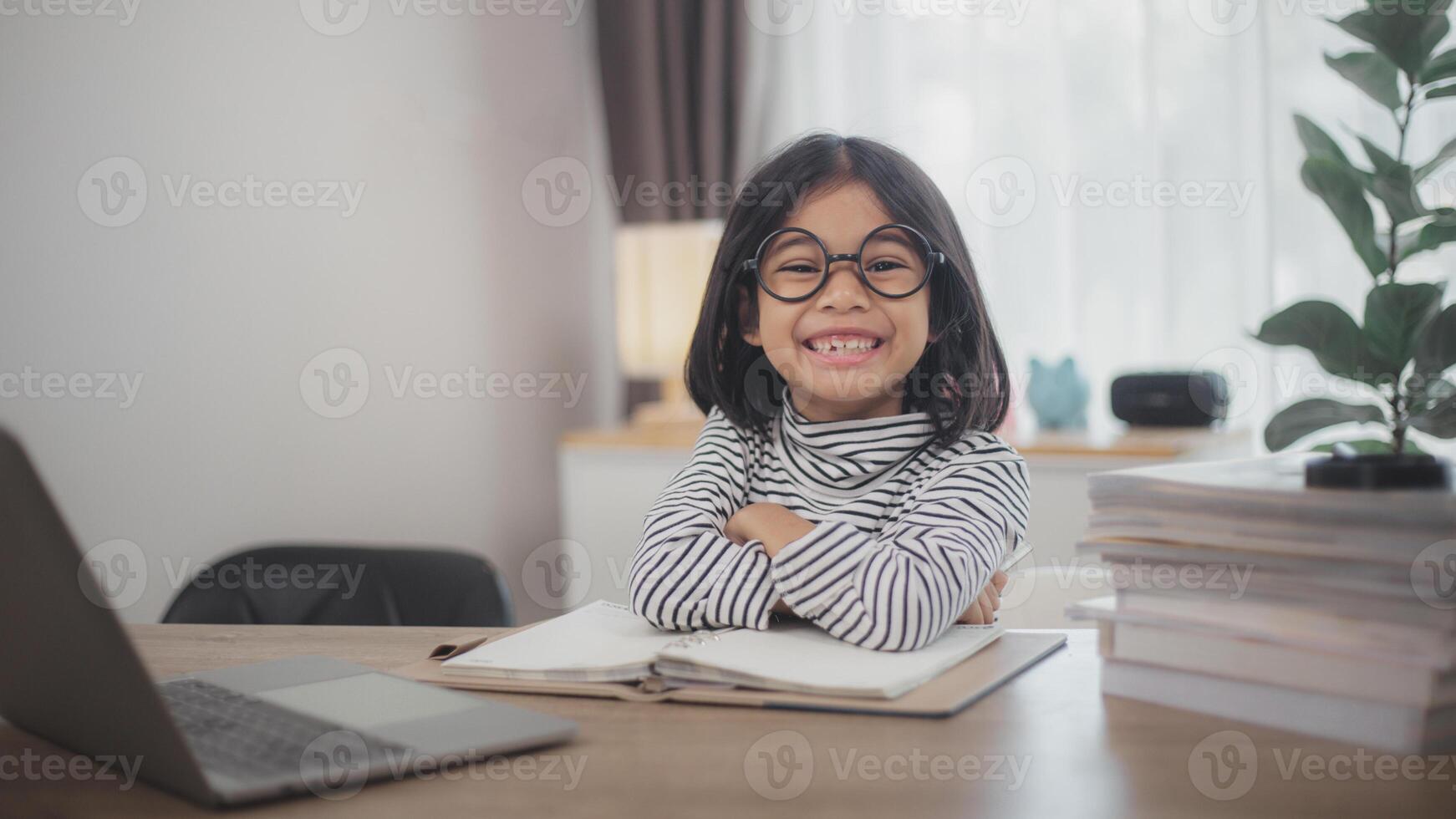 Happy little girl pupil studies online using a laptop at home, smiling small child recommend class or lesson. photo