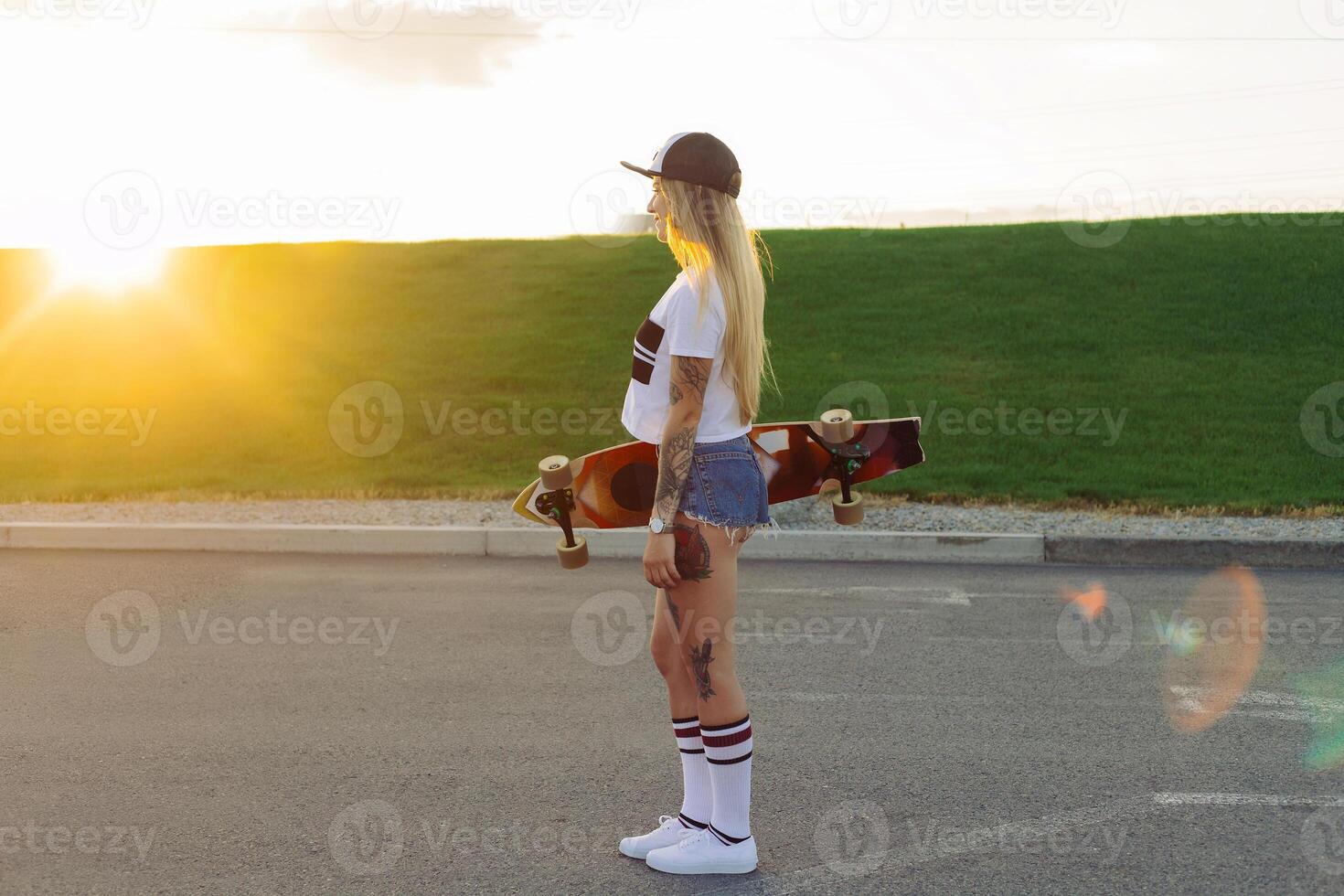 retrato de un hipster joven niña sonriente con un longboard a puesta de sol. foto