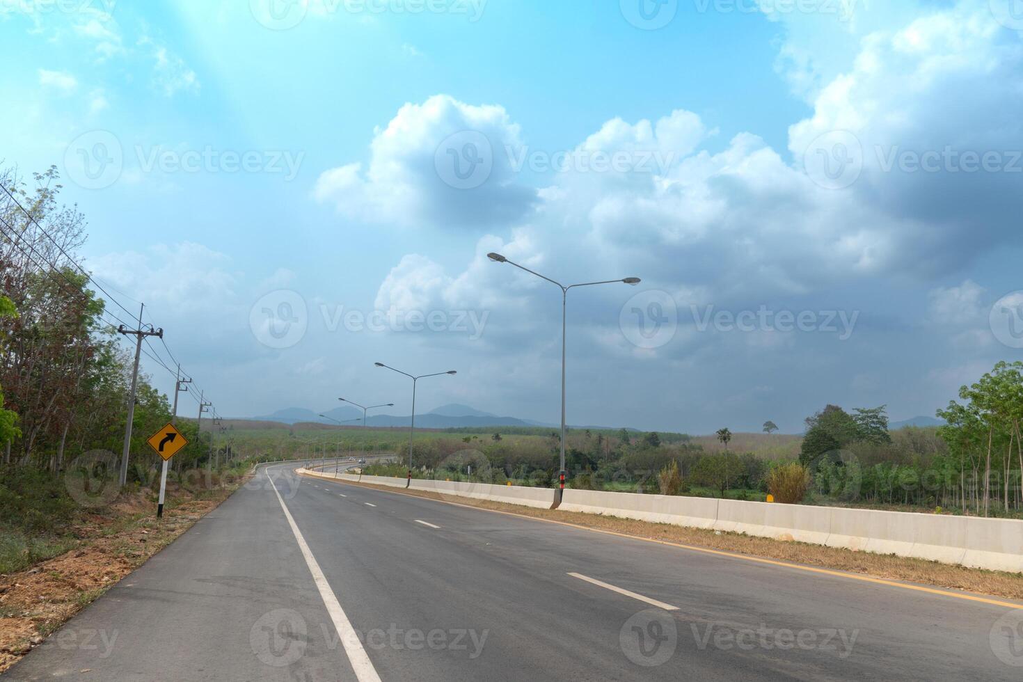 curvo asfalto la carretera con guarda lente y arboles en al lado de. debajo azul cielo en el campo de tailandia ligero brillante mediante el oscuridad de el arboles foto