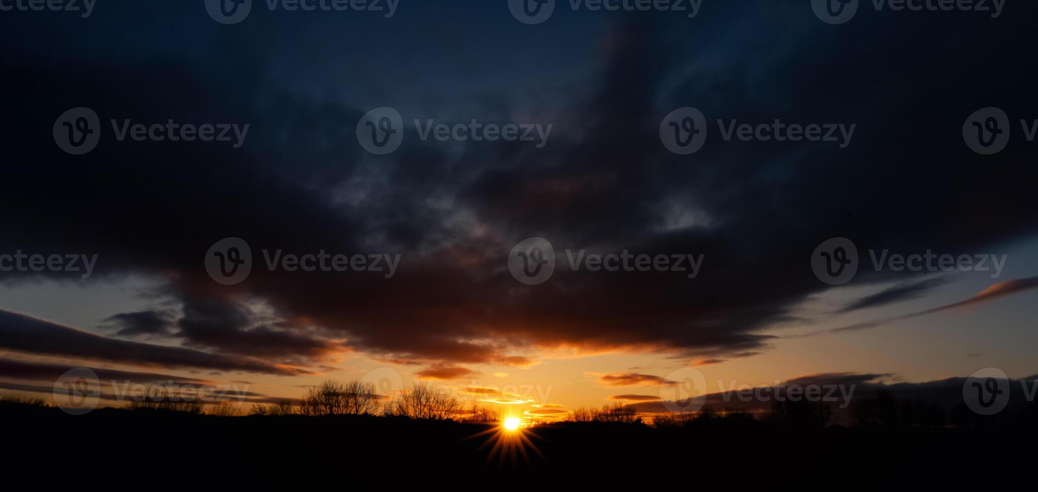 Sunset blue sky,Cloud Behind Silhouette Forest Tree in Evening Autumn,Winter Forest Field with Bright Sunrise Sky and gloomy cloudy.Countryside Landscape Under Scenic Colorful Sky with Sun Sun Dawn photo