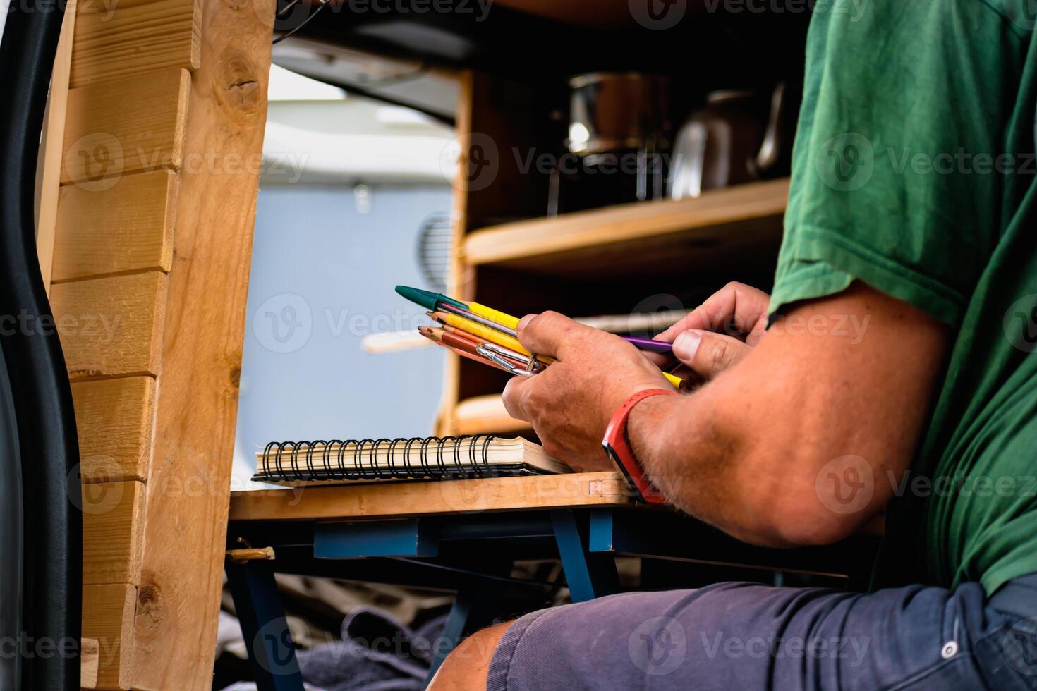 Man drawing on a notebook and holding pencils on a table in a converted van photo