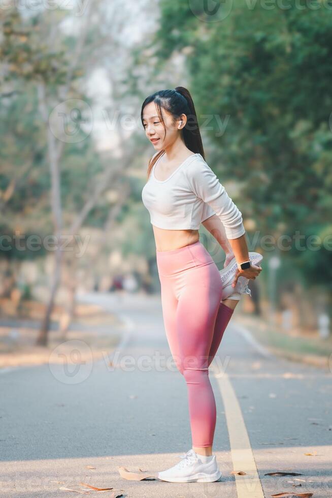 Fitness concept, Fit young female runner stretching her leg during a warm-up in a sunny park pathway. photo