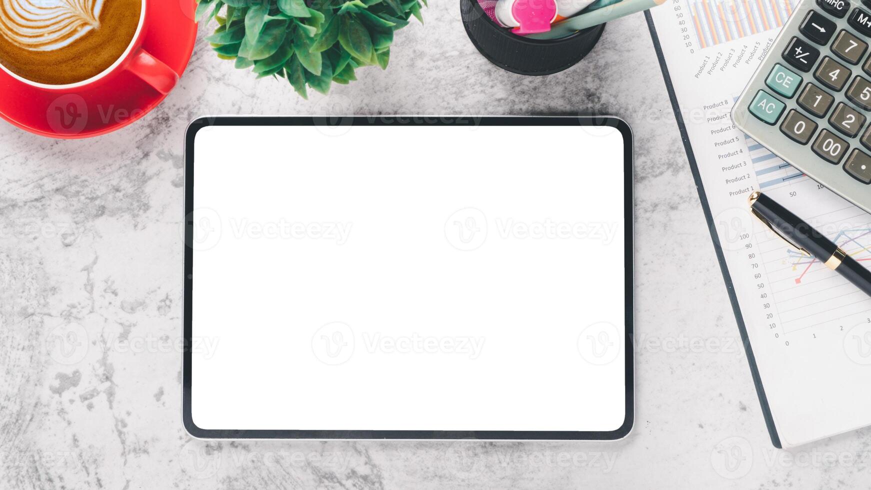 An empty tablet screen centered on a marble desk surrounded by a coffee cup, plant, stationery, and business documents. photo
