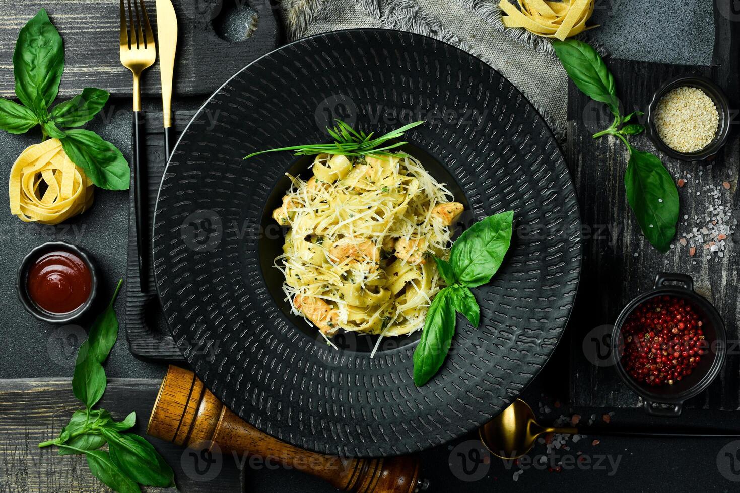 Pasta with pesto sauce and chicken in a black bowl. On a dark background, close-up. photo